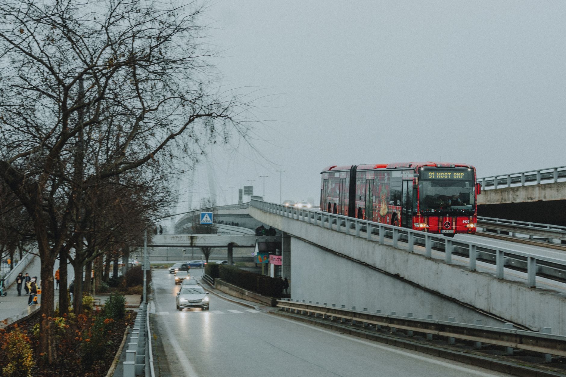 A modern public transport bus travelling along a dedicated busway lane towards a city skyline