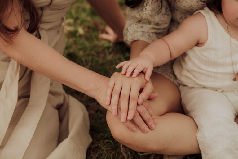 A supportive family carer holding the hand of an elderly family member in a sunny New Zealand home living room