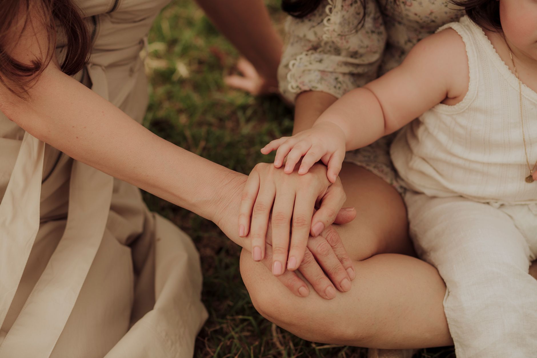 A supportive family carer holding the hand of an elderly family member in a sunny New Zealand home living room