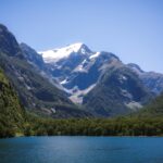 Fiord landscape in New Zealand with a snow-capped peak, forested cliffs and calm water