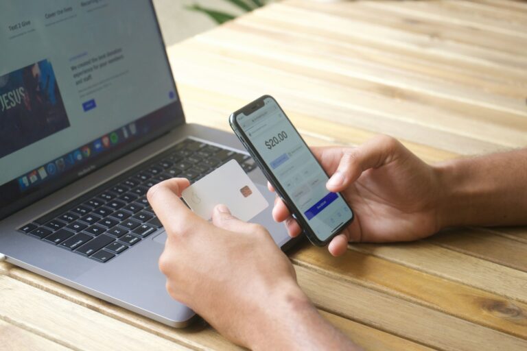 Person comparing an online money transfer on a smartphone with a laptop and bank card on a table