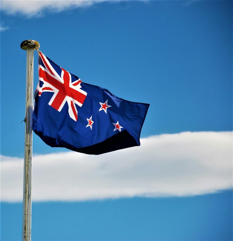 The New Zealand flag flying on a flagpole against a blue sky with clouds